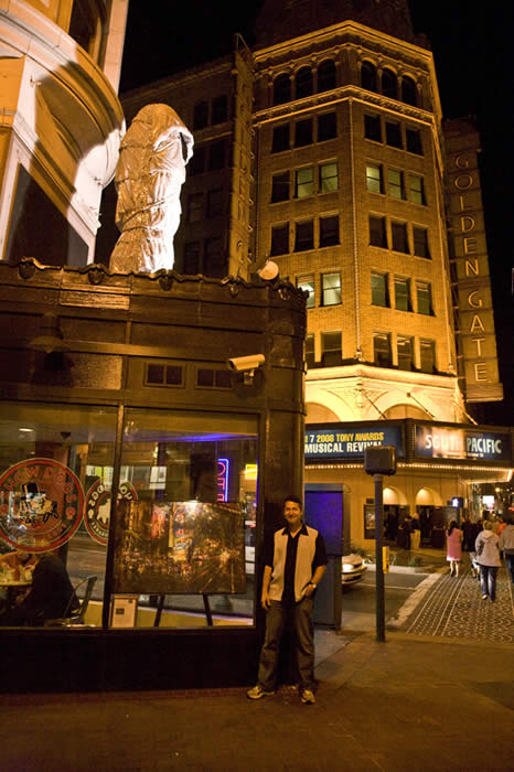 View of the painting with the Golden Gate Theater in the background. The mysterious wrapped figure on the roof is part of the Arts in Storefronts program.